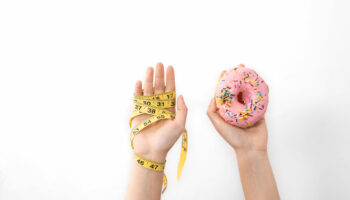 Hands hold a donut and a measuring tape on a white background, the concept of choice in nutrition, weight loss, diet, obesity, overeating.